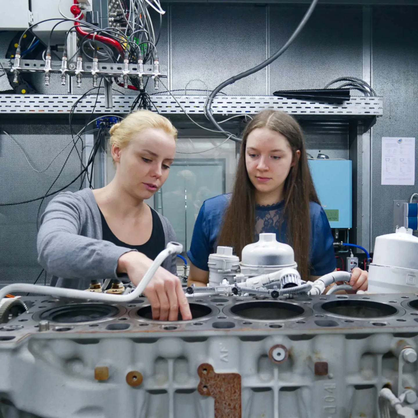Anna Rhode und eine Kollegin arbeiten gemeinsam an einem Motorblock im Prüfstand