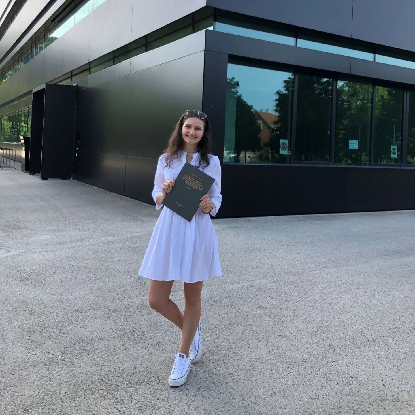 Ines Braun steht vor einem modernen Gebäude und hält ihre Abschlussmappe in den Händen