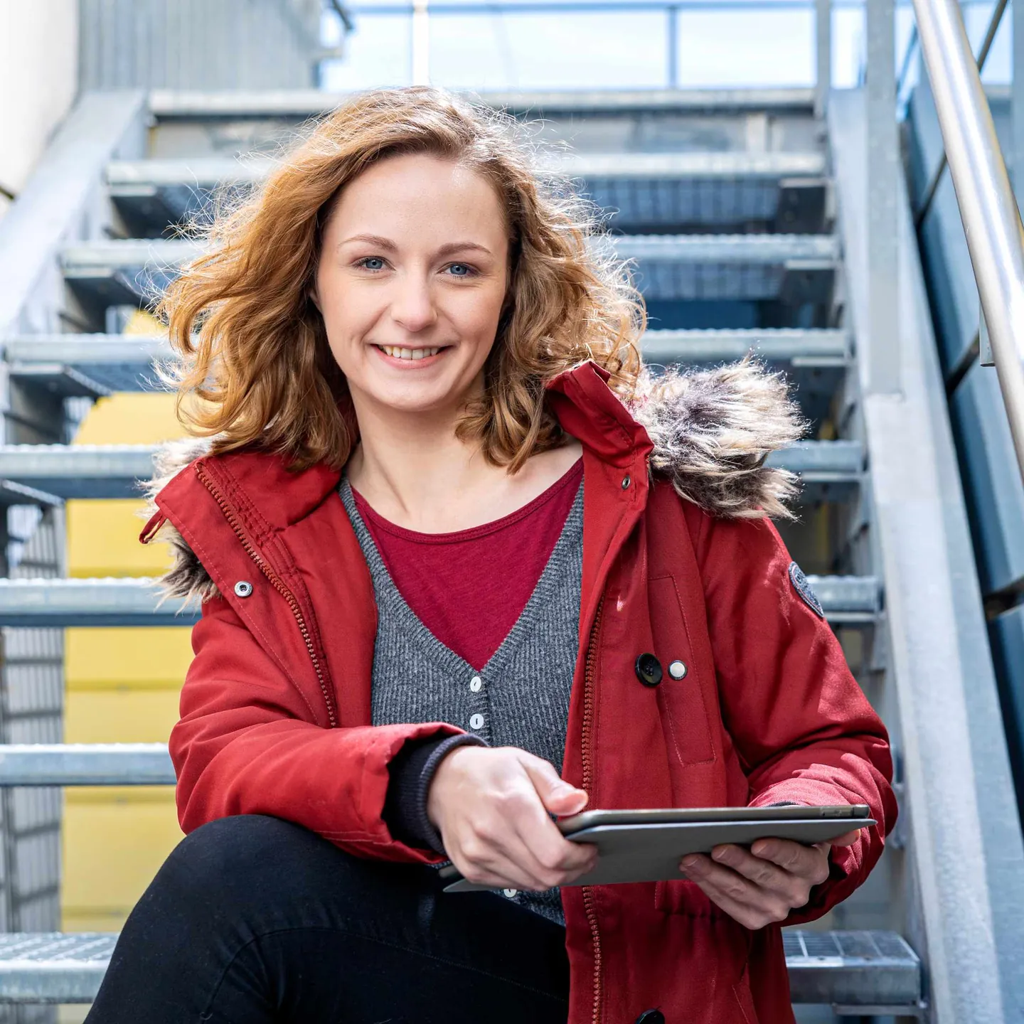 Marieluise Oden sitzt mit einem Tablet in der Hand auf einer Metalltreppe