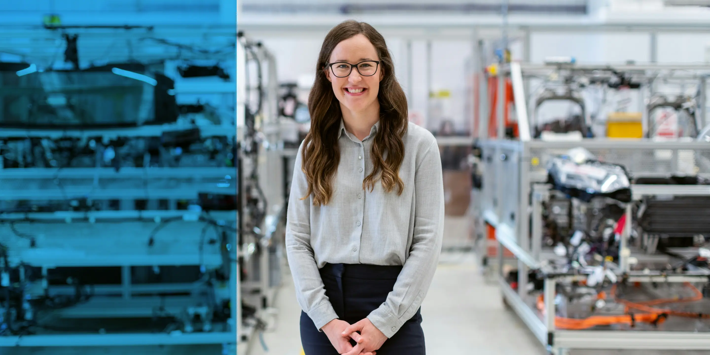 Junge Ingenieurin steht lächelnd in einer Werkhalle zwischen technischen Prüfständen